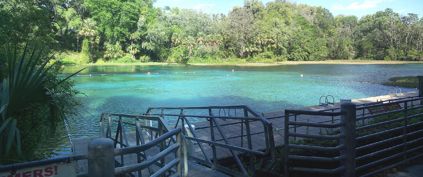 Wide teal swimming area with a wood dock rail in front
