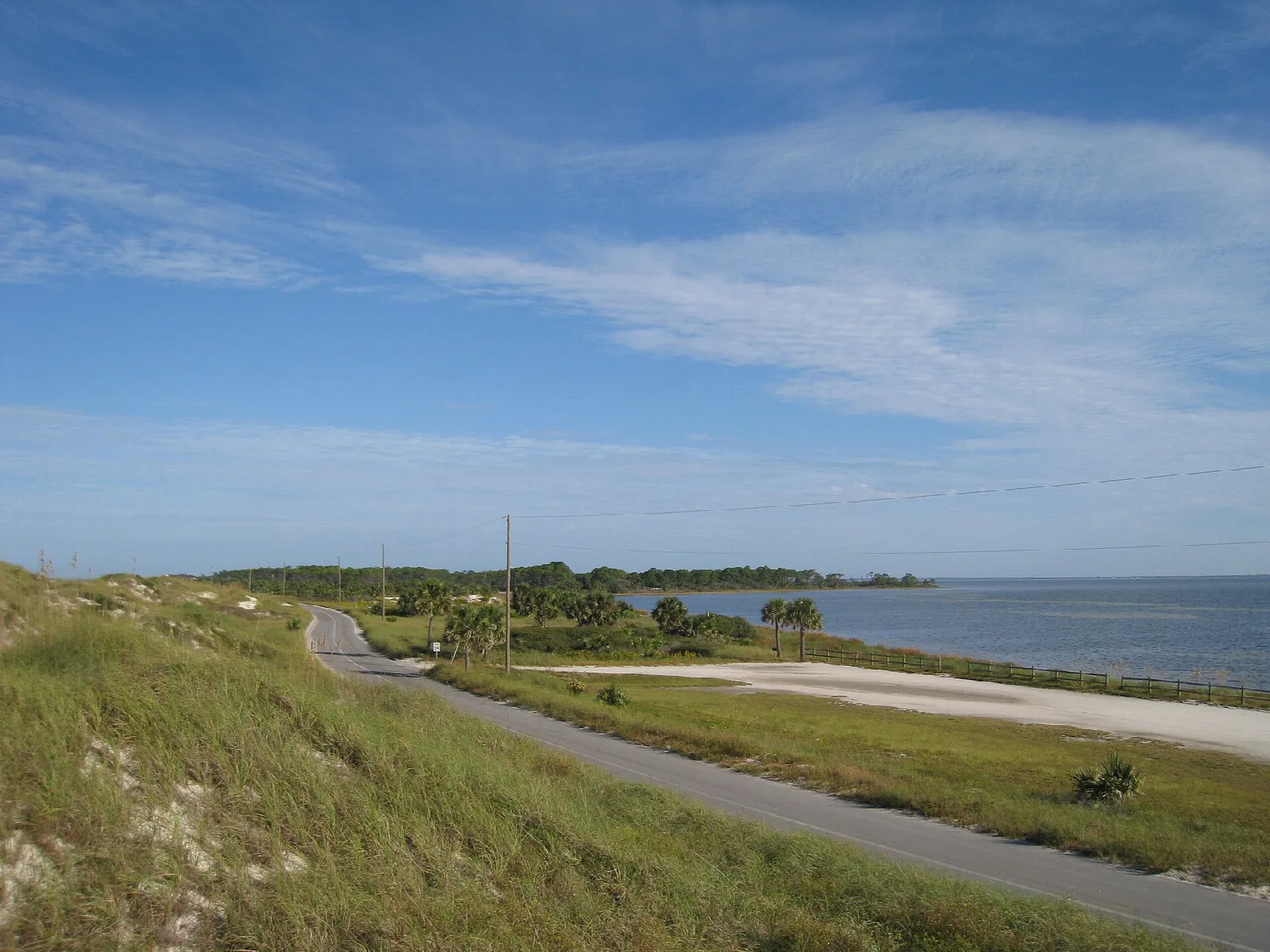 Paved road curving through dune grass beside the bay