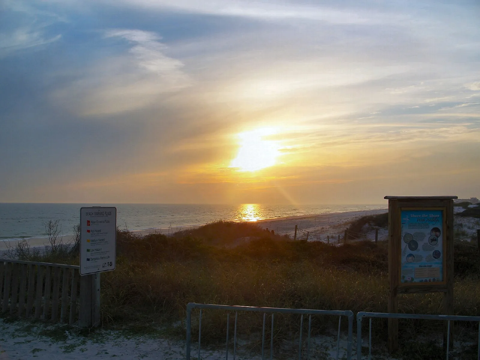 Sun setting over the Gulf above dune grass and signs