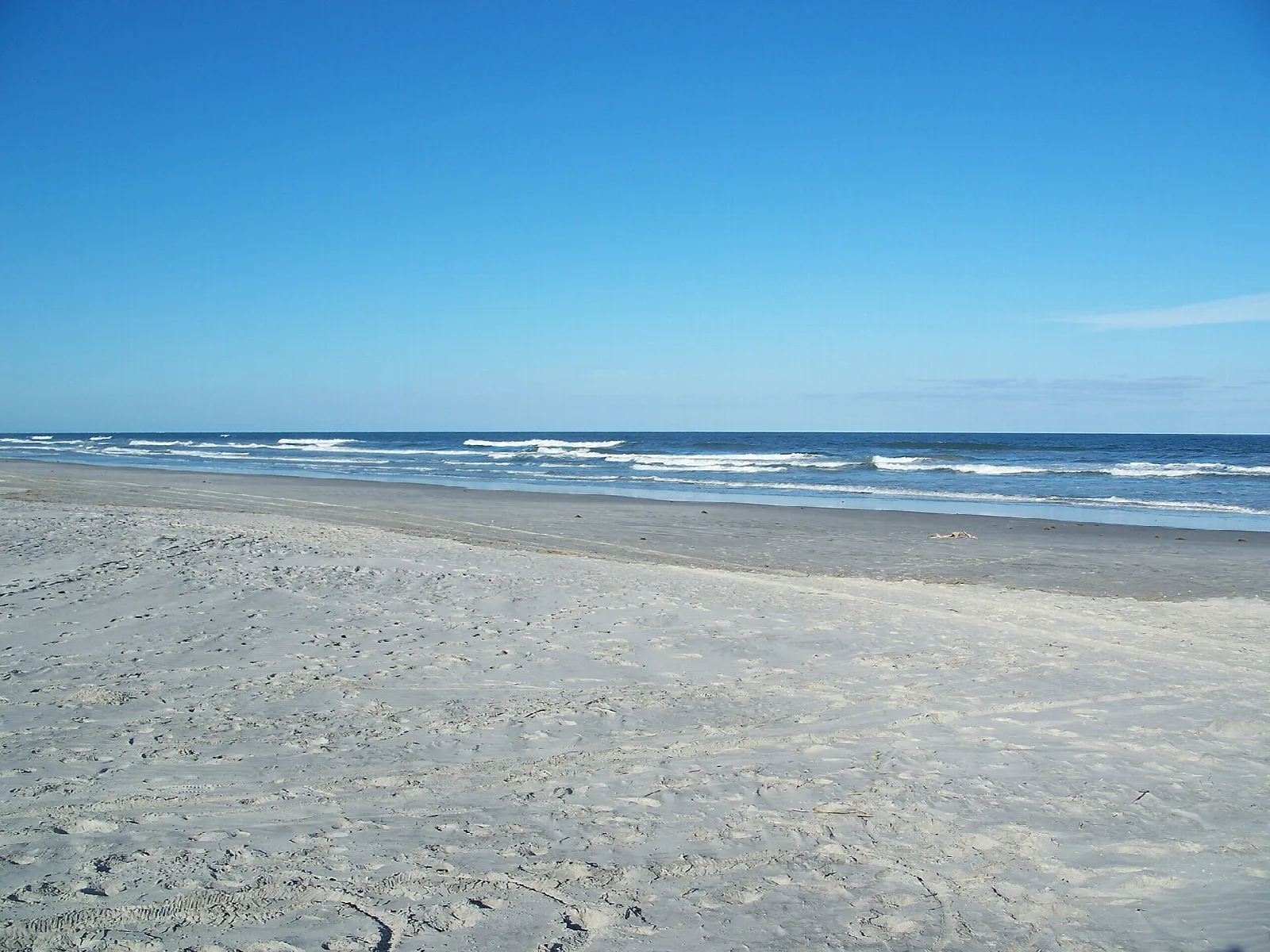 Pale sand beach and low surf under blue sky