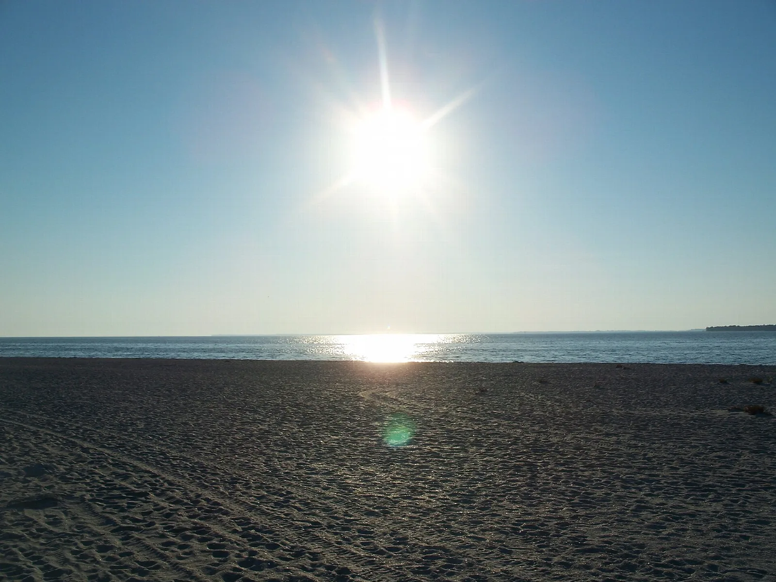 Dark sand beach with low sun over the water
