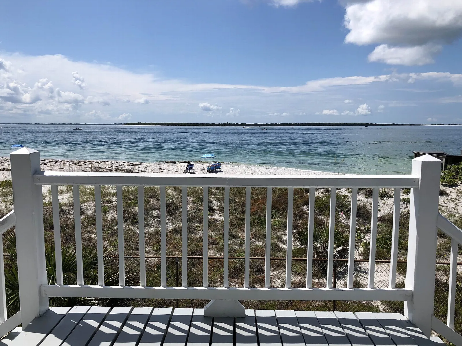 White railed deck overlooking a sandy beach and calm water