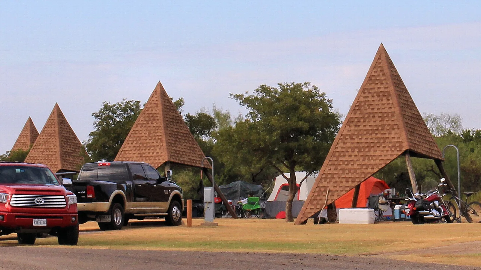 Pyramid-roofed camp shelters with trucks and tents on a grassy camping area