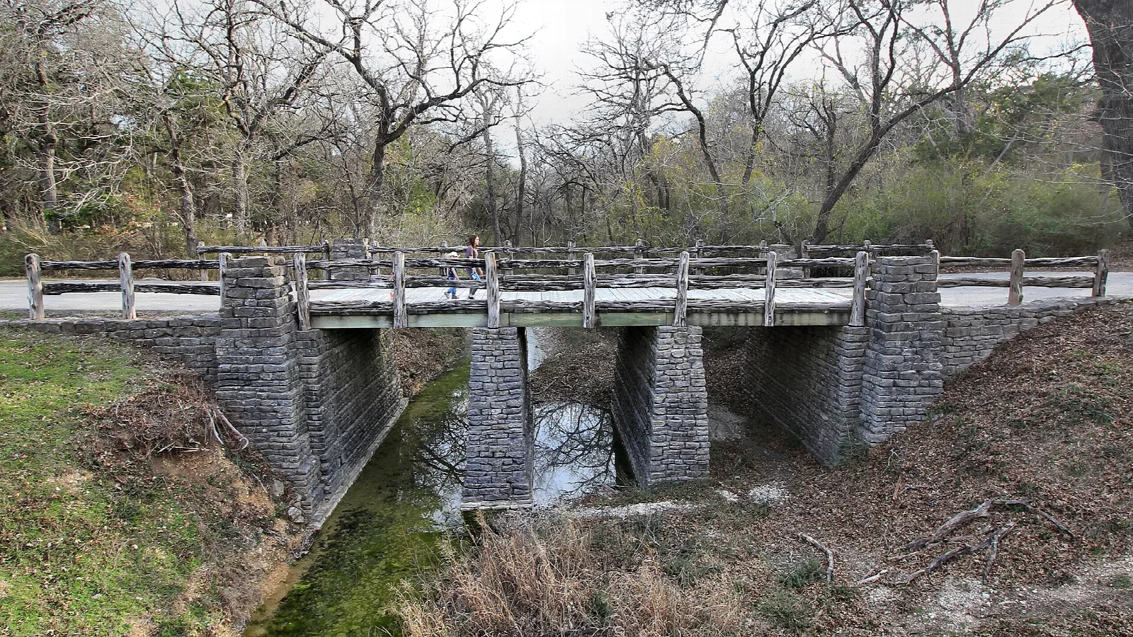 Stone bridge with wooden rails over a dry creek