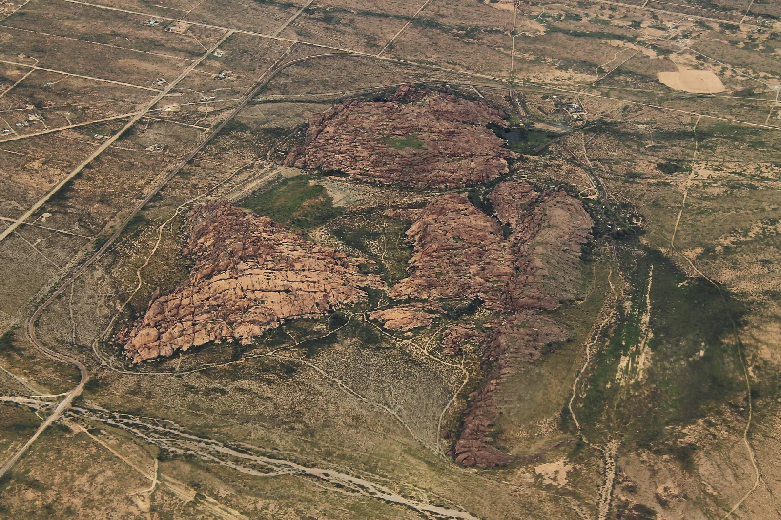 Aerial view of red rock hills in flat desert with dirt roads