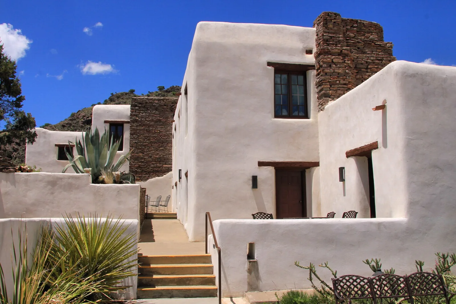 White adobe lodge exterior with stairs and agave plants