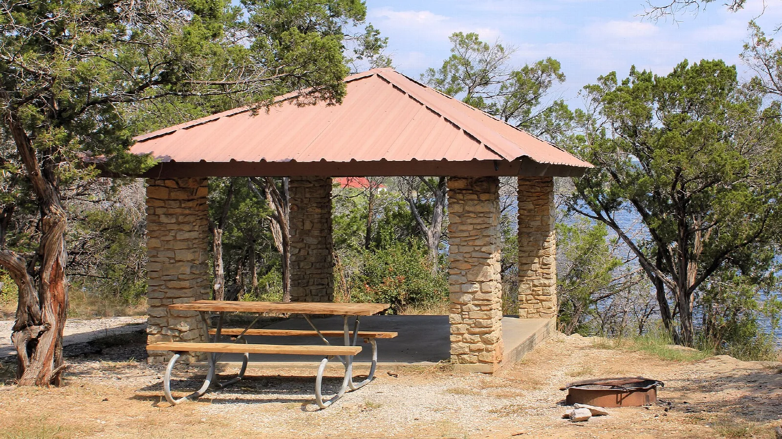 Stone picnic shelter with a table and fire ring among trees