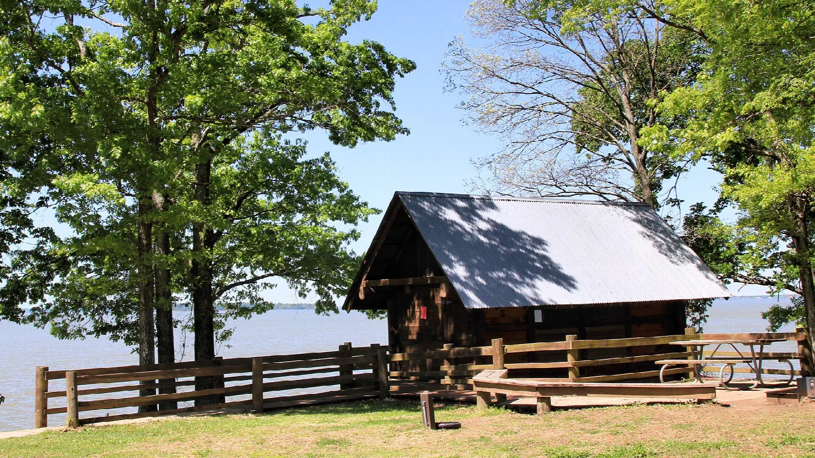 Small log cabin with a porch beside a lake and trees