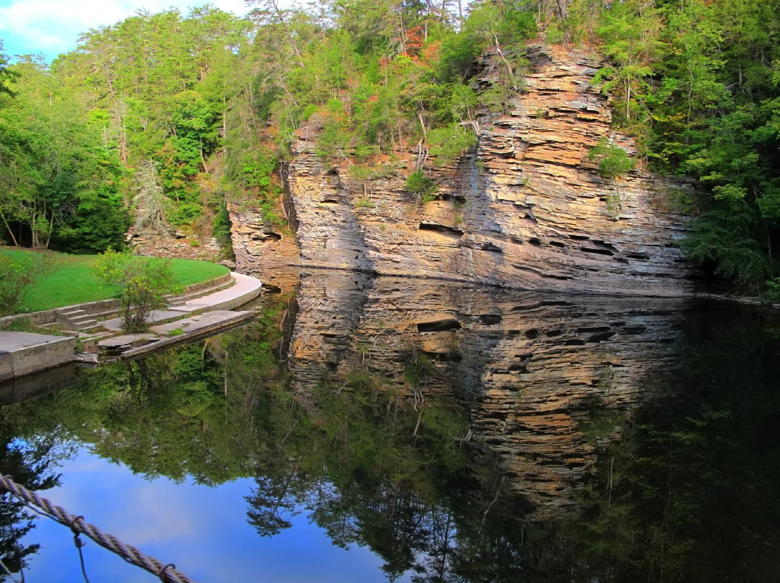 Sandstone bluff reflected in still water, with grass along the shore