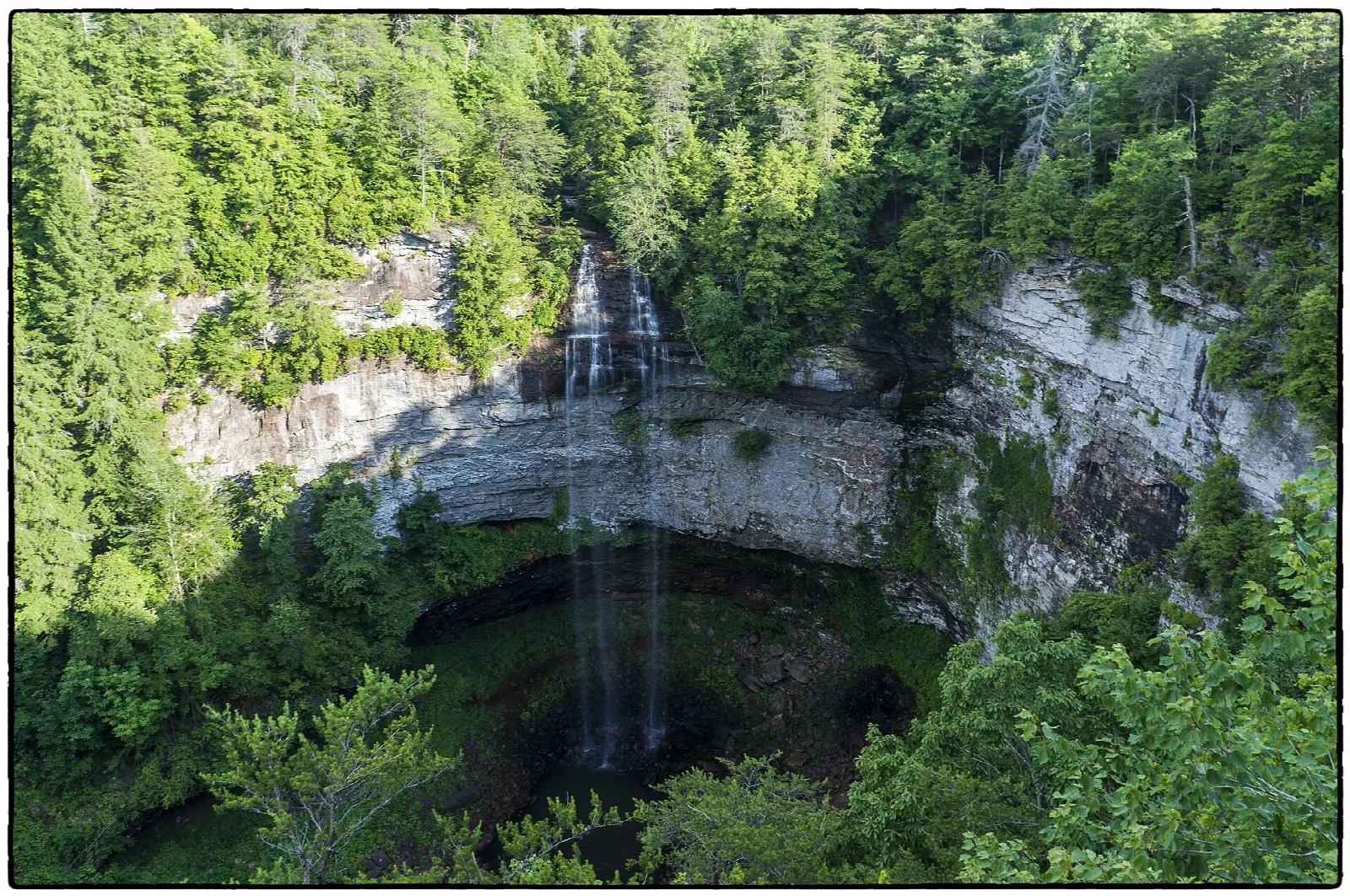 Waterfall pouring over a cliff into a forested gorge