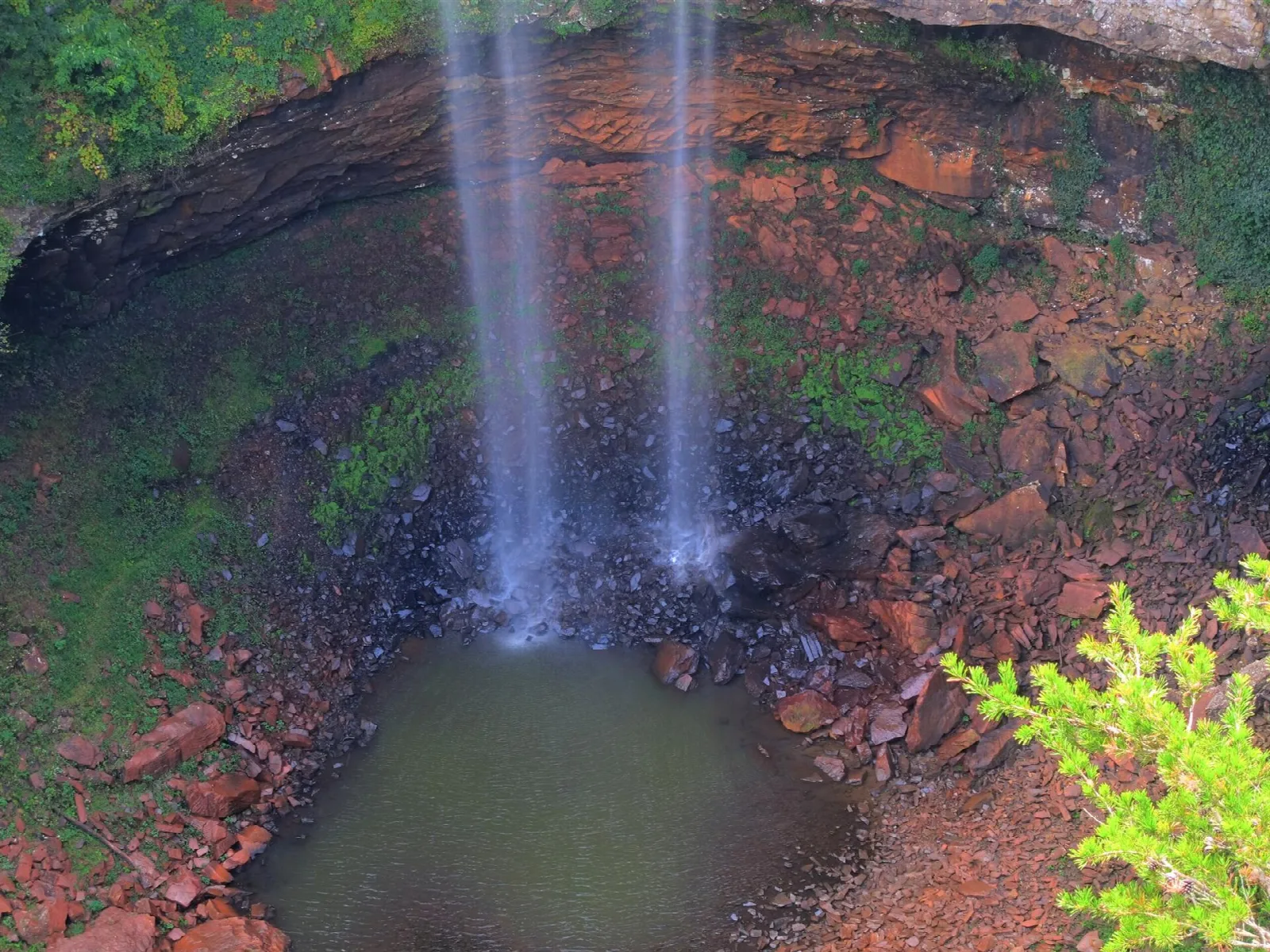 Twin waterfall streams falling into a small pool with red rocks