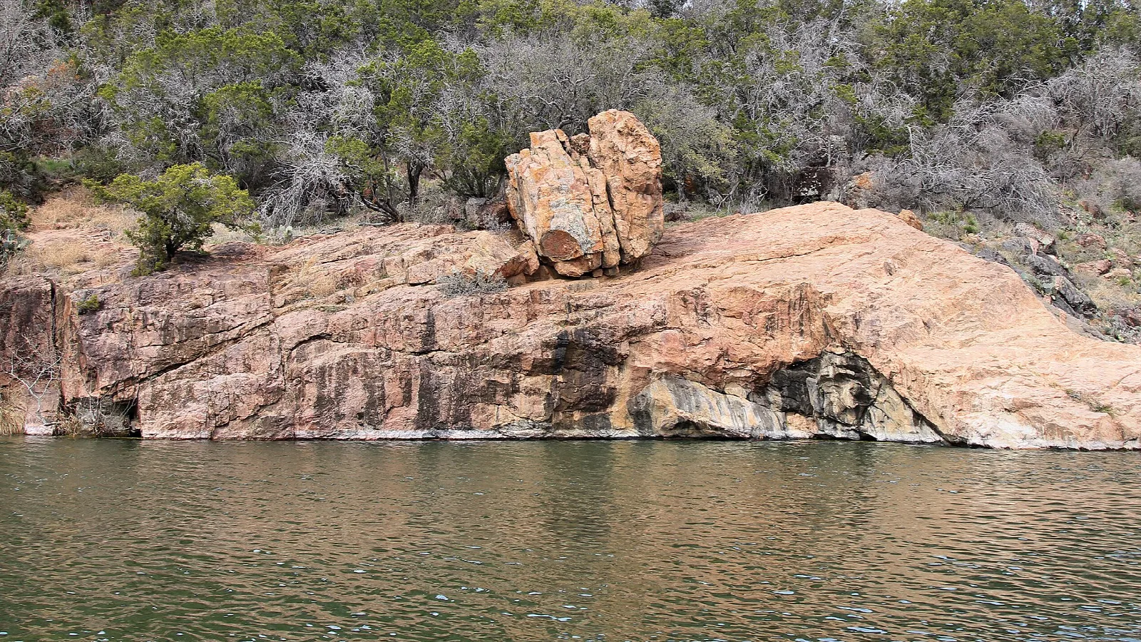 Pink granite shoreline with a boulder above still green water