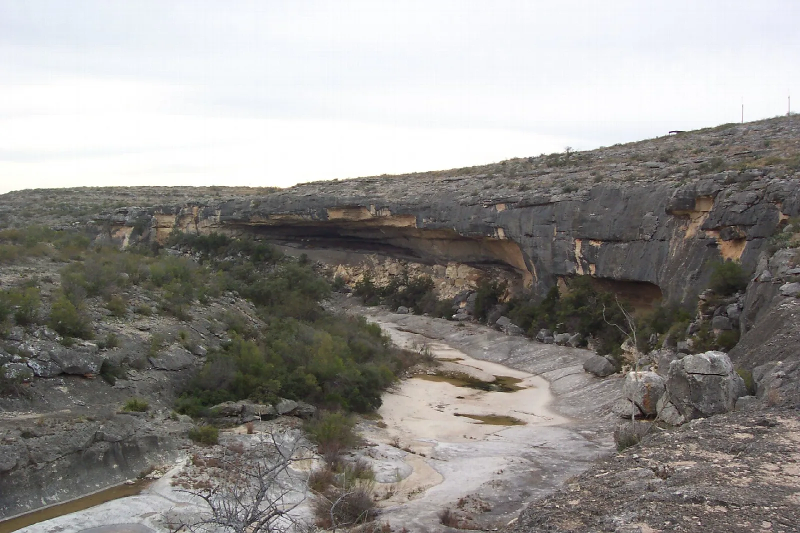 Dry riverbed below a layered limestone canyon wall