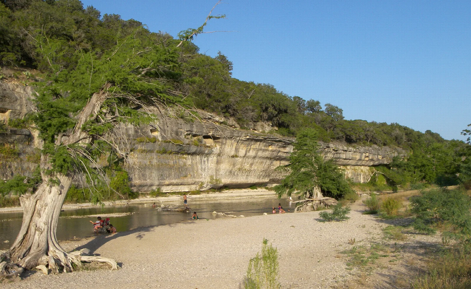 Pale limestone bluff above a gravel bar on the river, with cypress and blue sky