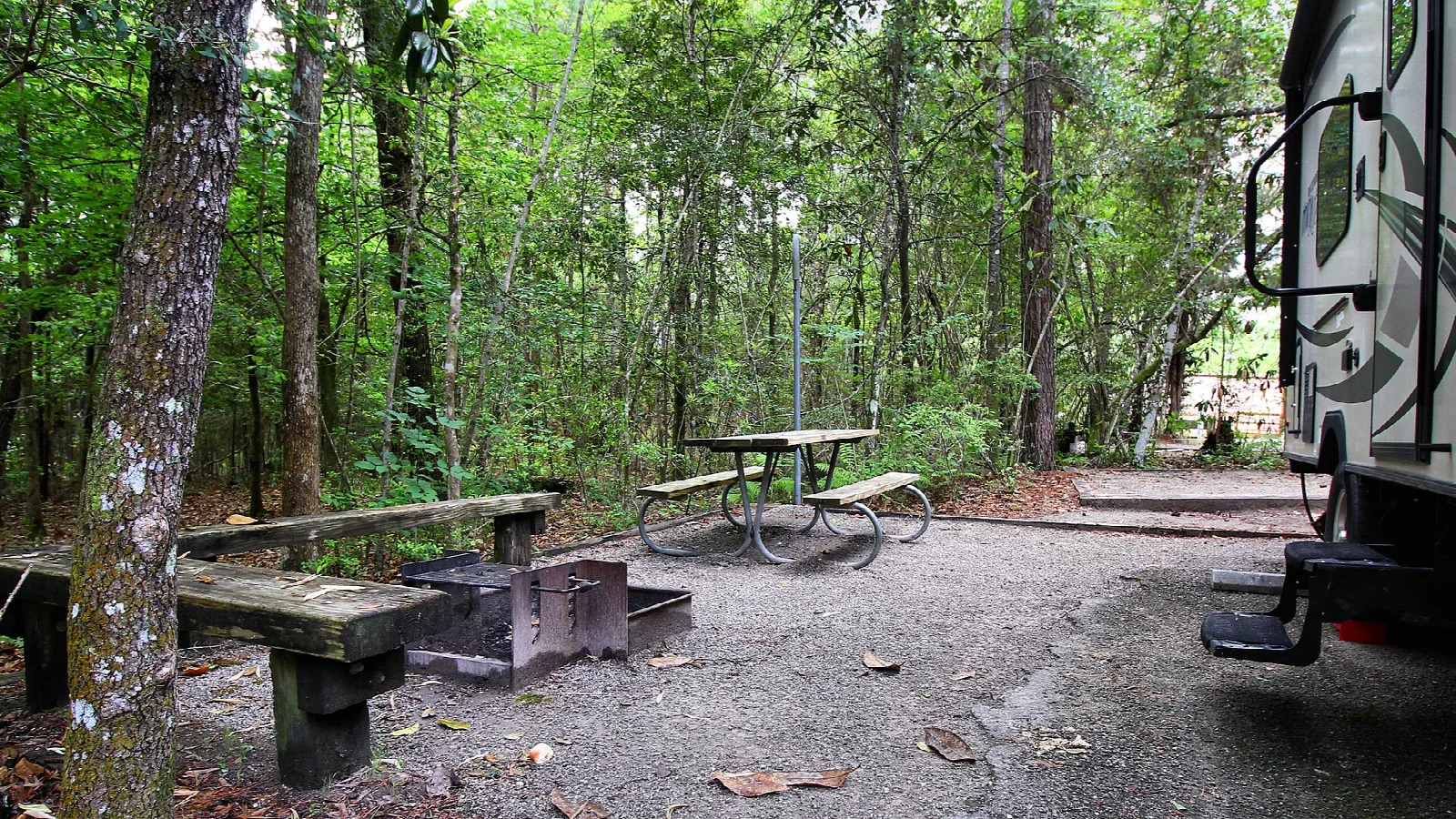 Campsite with picnic table, fire ring and an RV on a gravel pad in the woods
