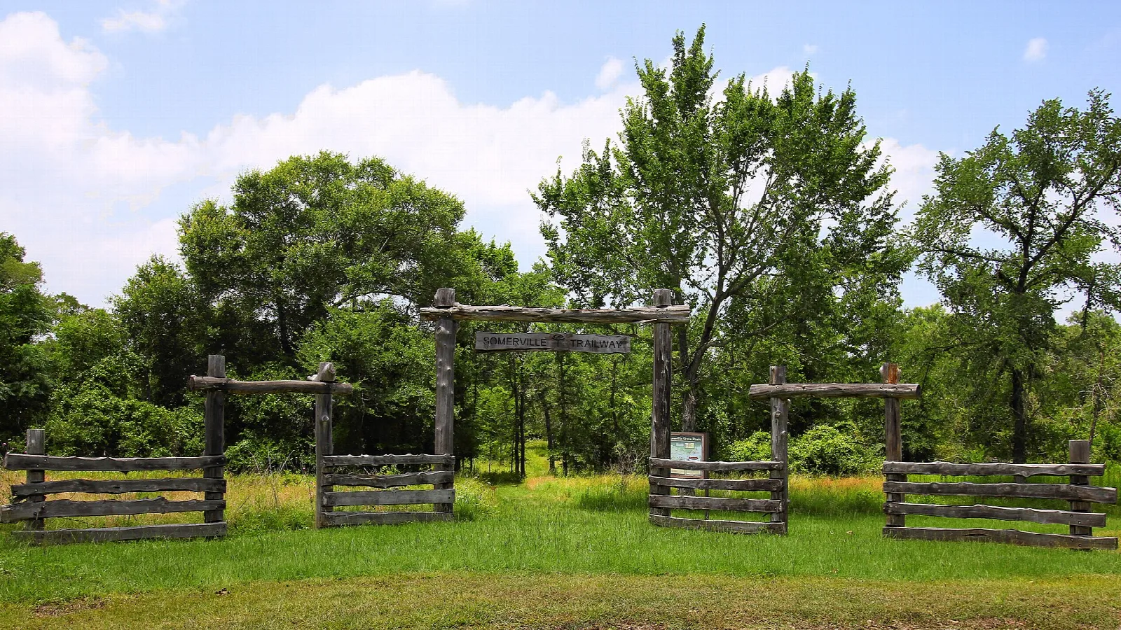 Wooden rail gate and fence at a trailhead in a grassy clearing