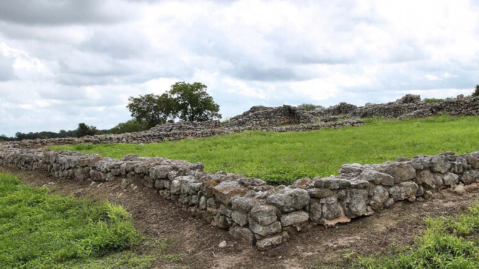 Low stone wall ruins running across a grassy field under cloudy sky