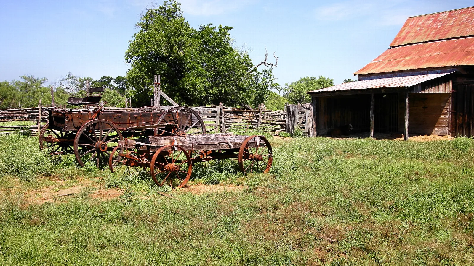 Old farm wagons beside a barn with a red roof
