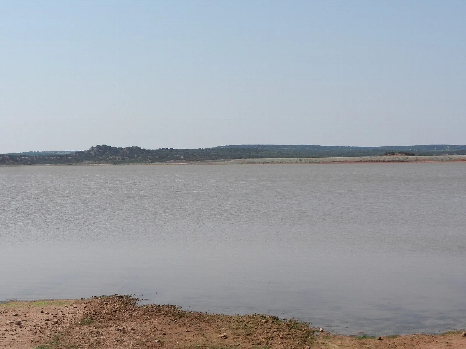 Wide calm lake under a pale sky with low hills beyond