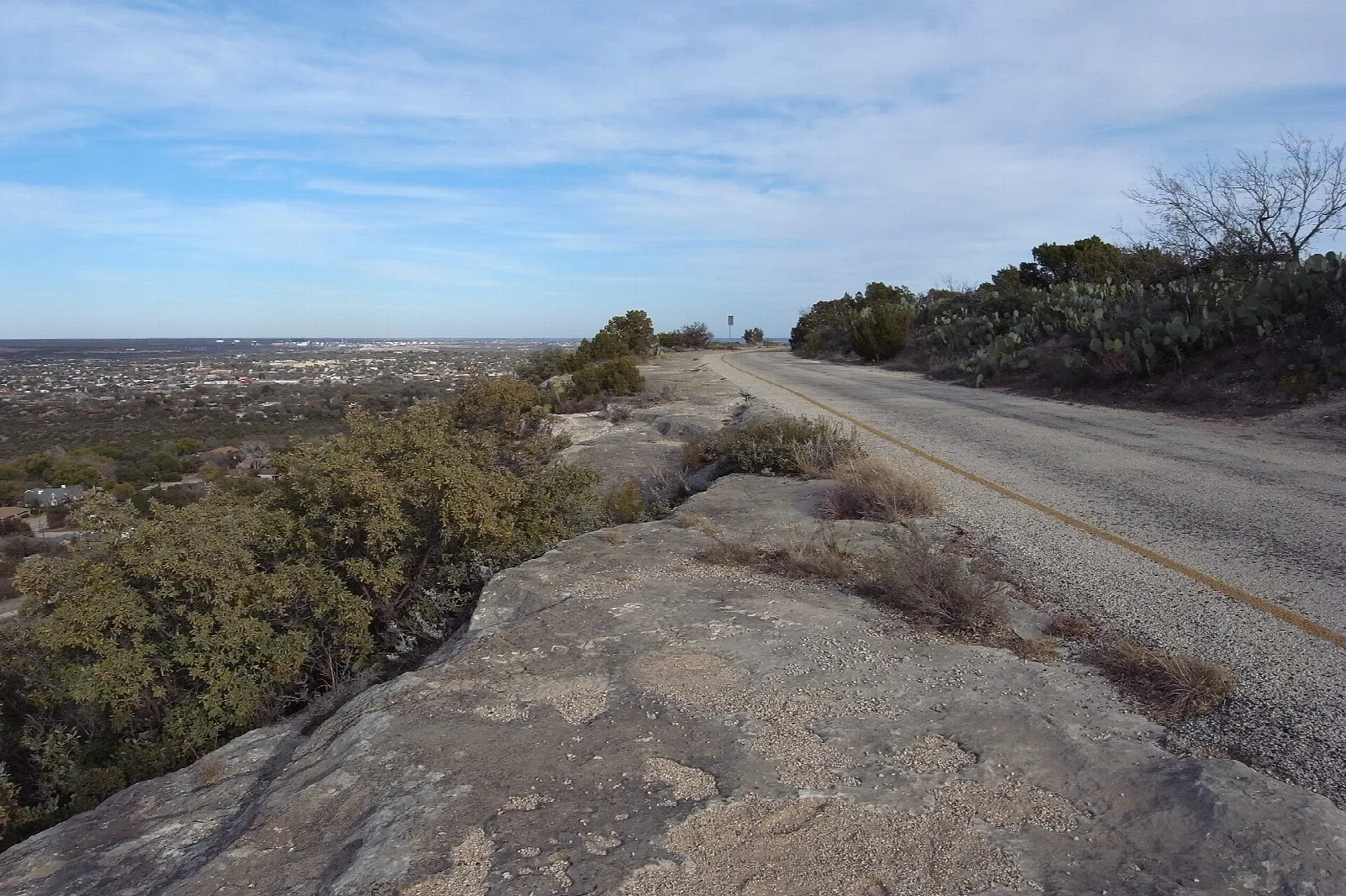 Paved road curving over bare rock through scrub brush