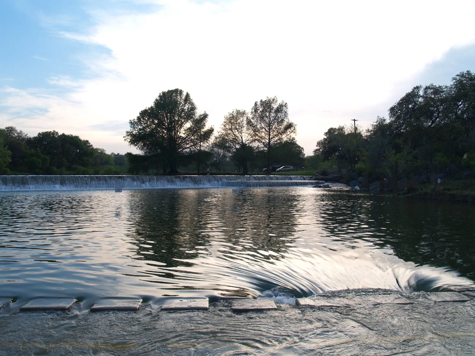 Low dam with water spilling across a river at dusk