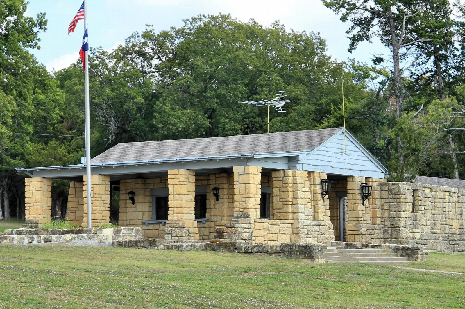 Stone and wood headquarters building with a covered porch and a flag, set on a lawn