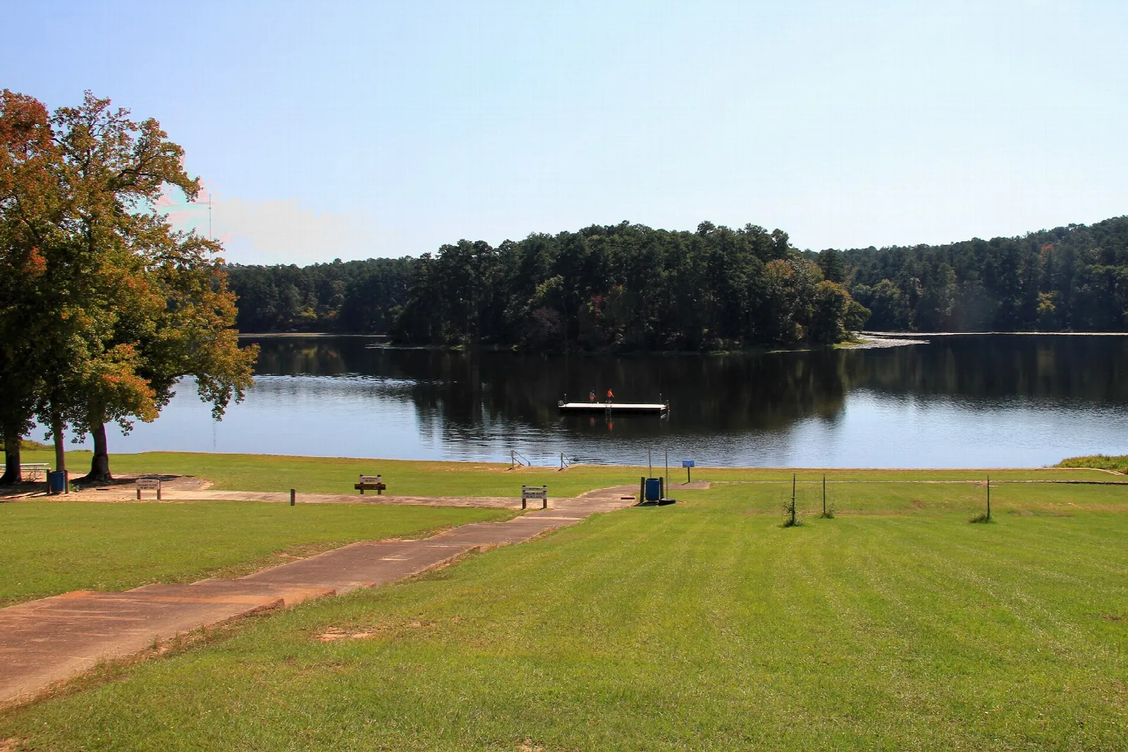 Mowed lawn sloping down to a lake with trees across the water and a swim area