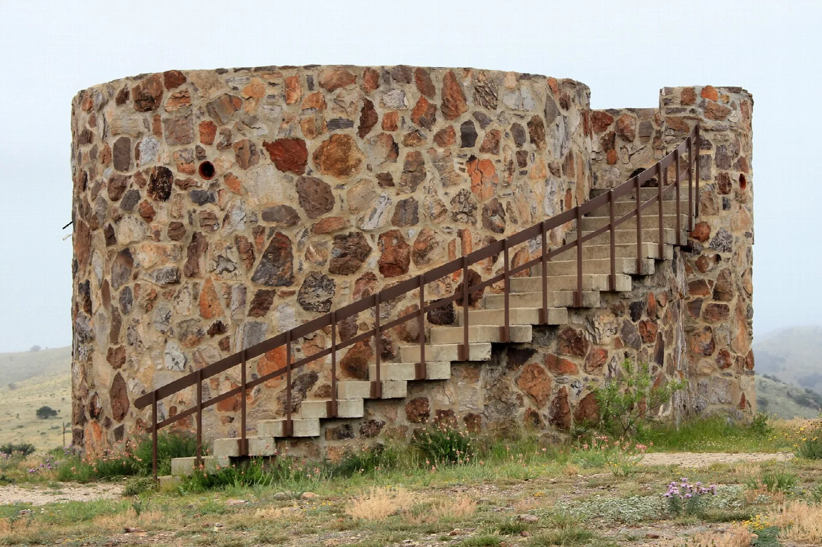 Round stone tower with an outside staircase and railing on open ground