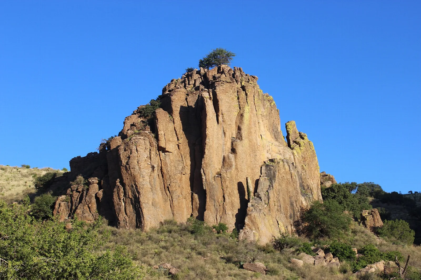 Tall brown rock outcropping on a hillside under a clear blue sky