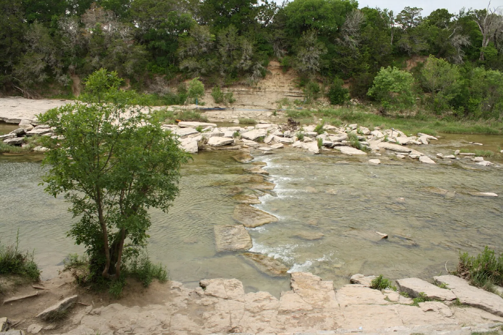 Shallow river crossing over flat rock ledges with green trees behind