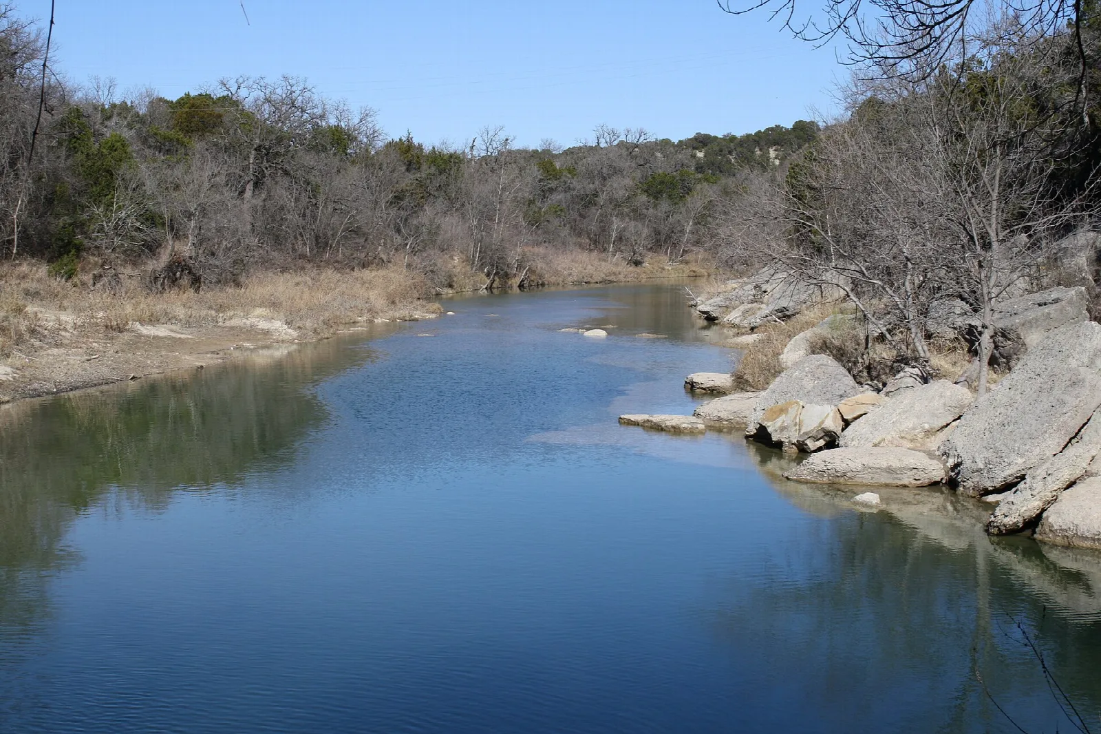 Blue river bending past rocky banks with trees on both sides