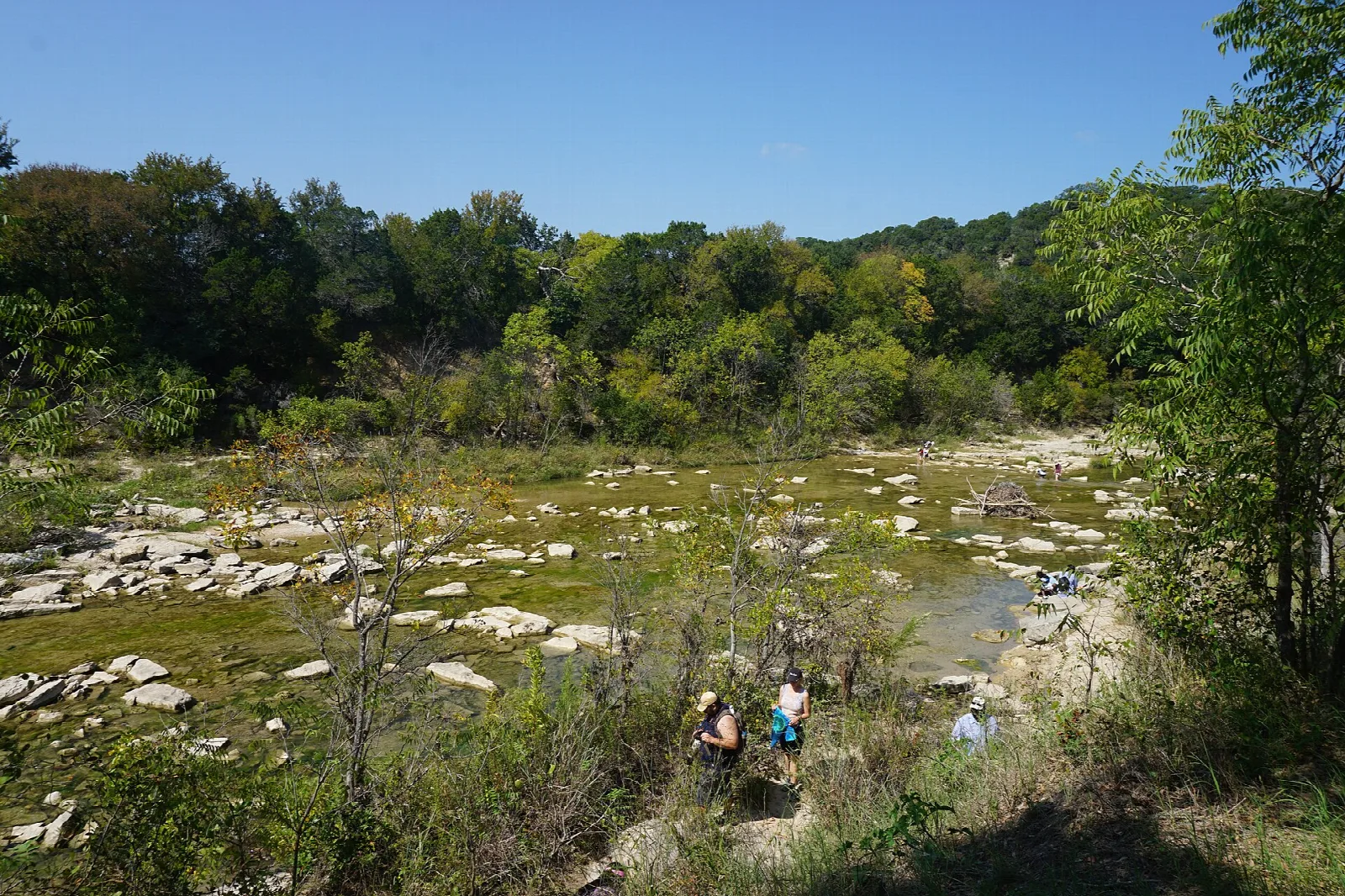 Shallow river over flat rock with a few people wading and trees behind