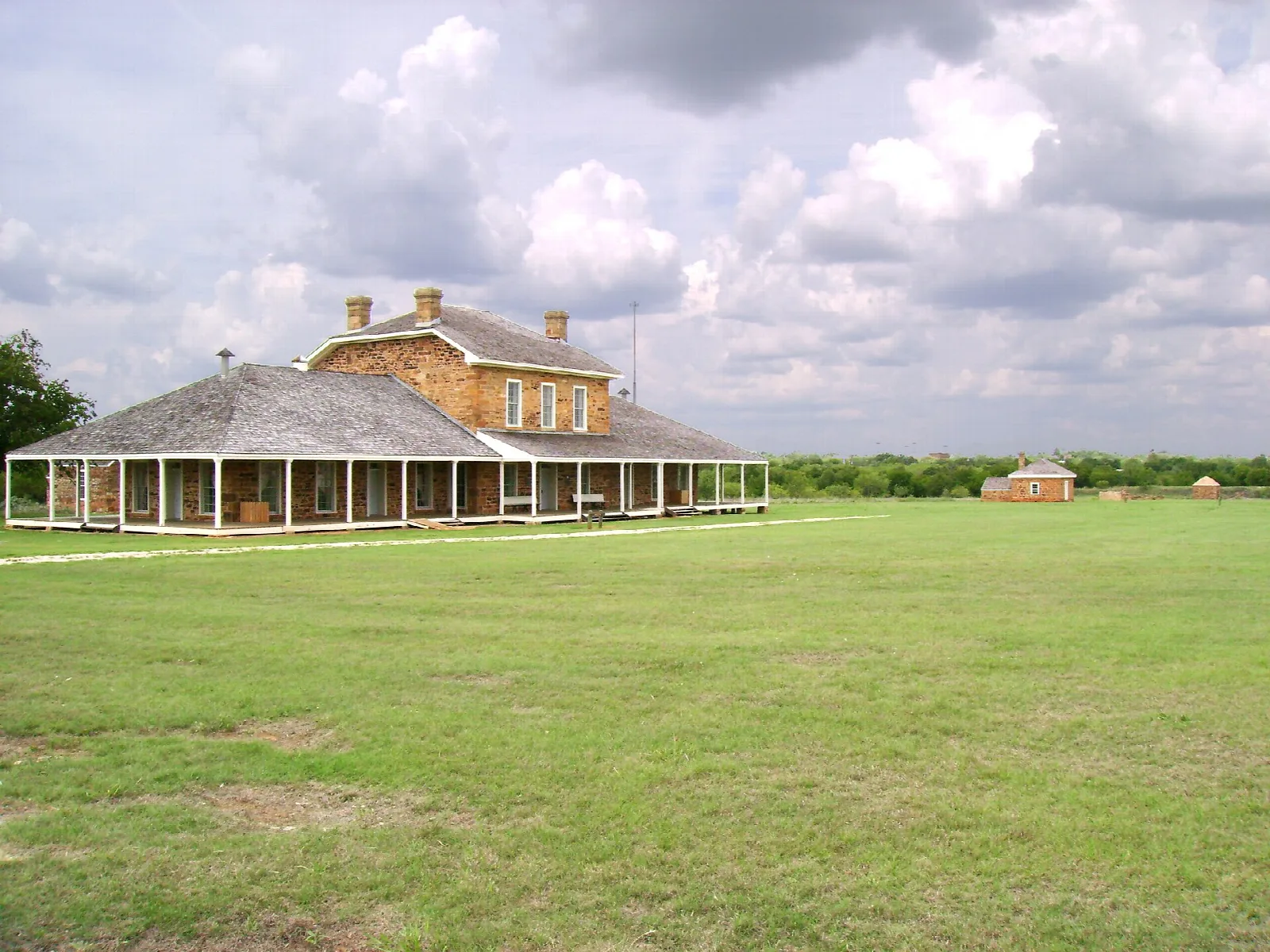 Stone hospital building and other old fort buildings across a wide green parade ground