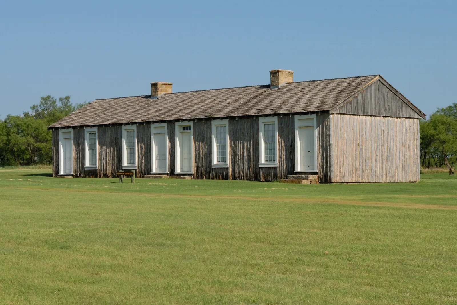 Long weathered wood barracks building on a grassy field