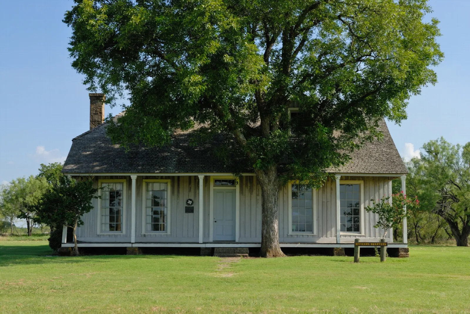 White wood officer quarters beside a large shade tree