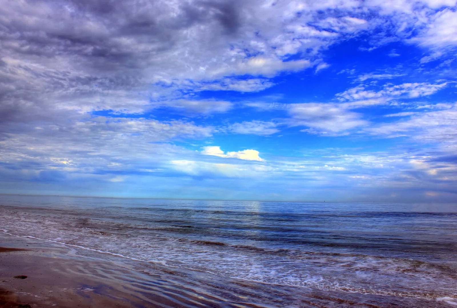 Gulf beach with wet sand and waves under a dramatic blue sky with clouds