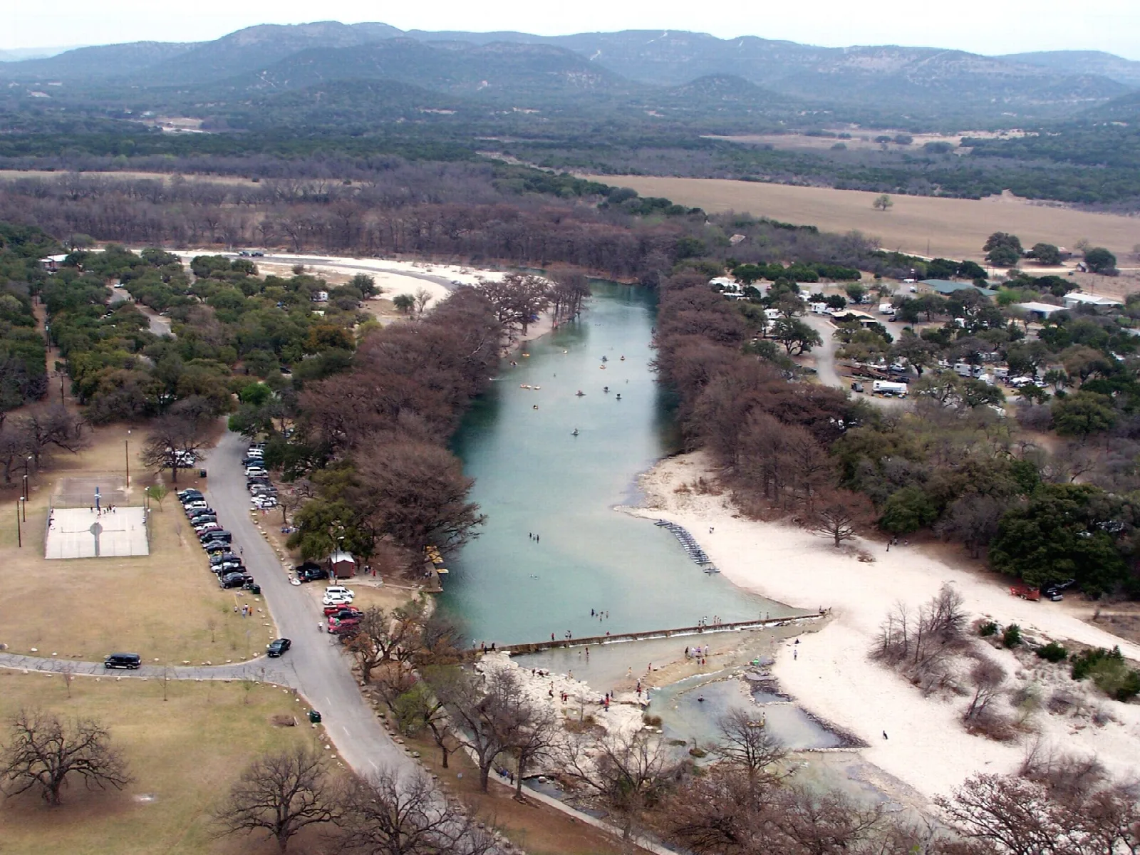 Aerial view of a green river with a sandy beach and park buildings