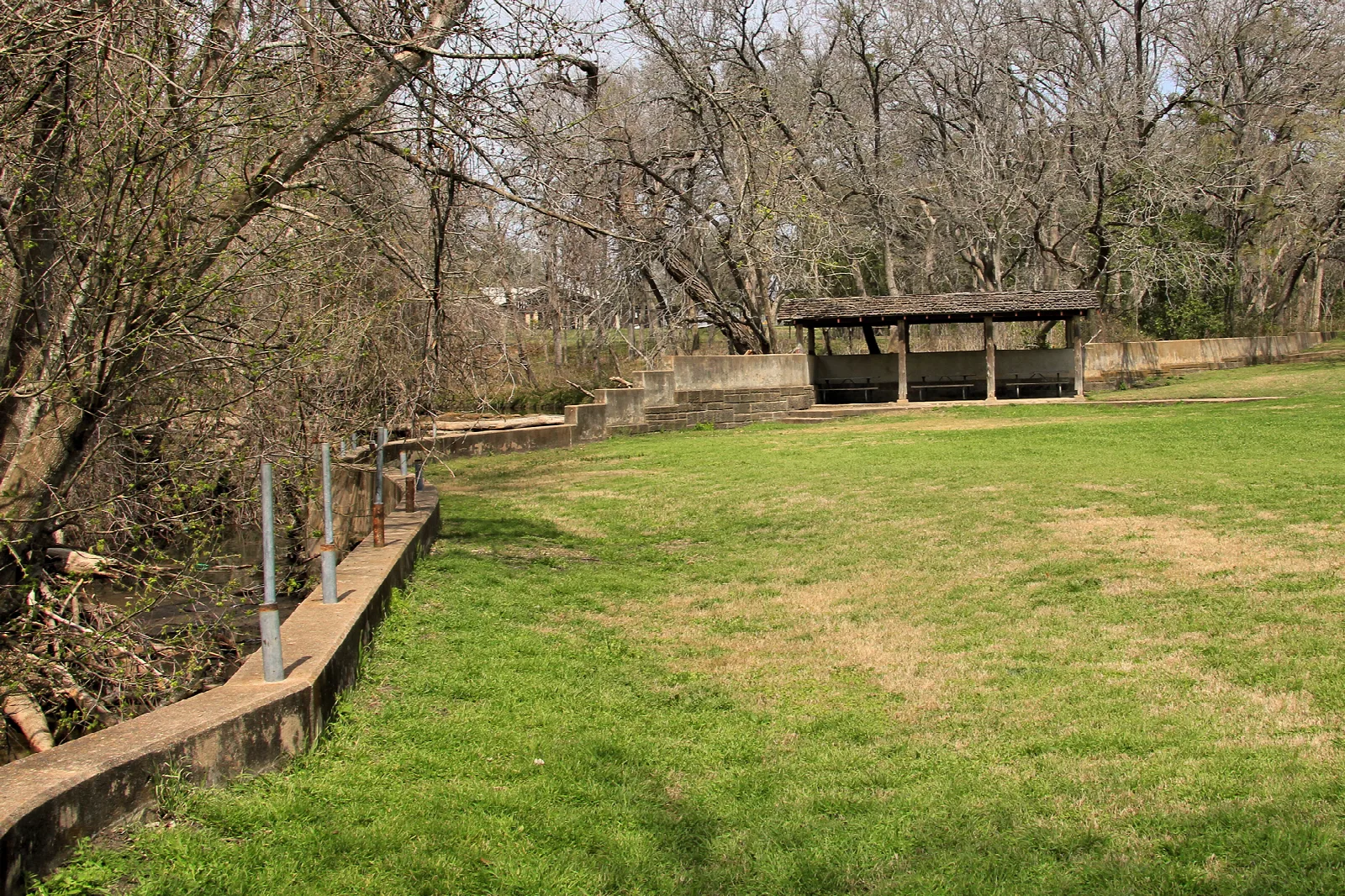 Grass lawn beside an old stone pool wall with a small shelter