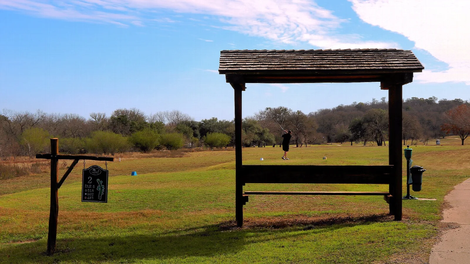 Golf tee box with a wooden shade shelter on a green course