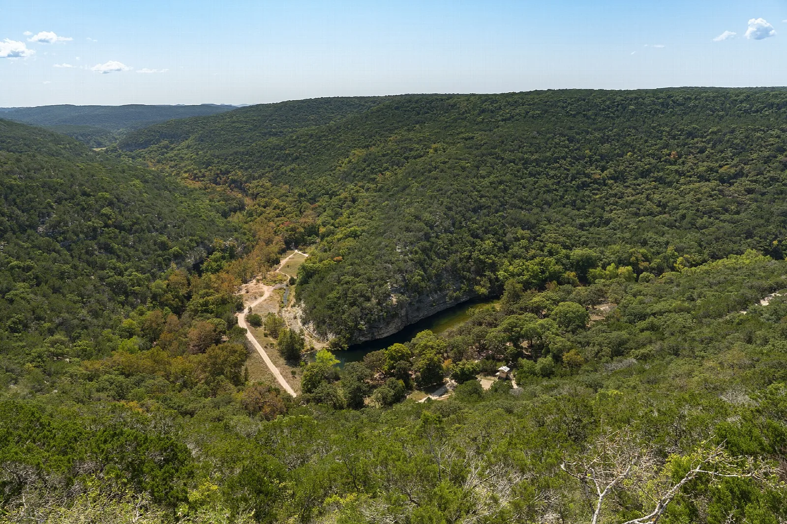 Forested canyon hills with a dirt trail winding along the valley floor