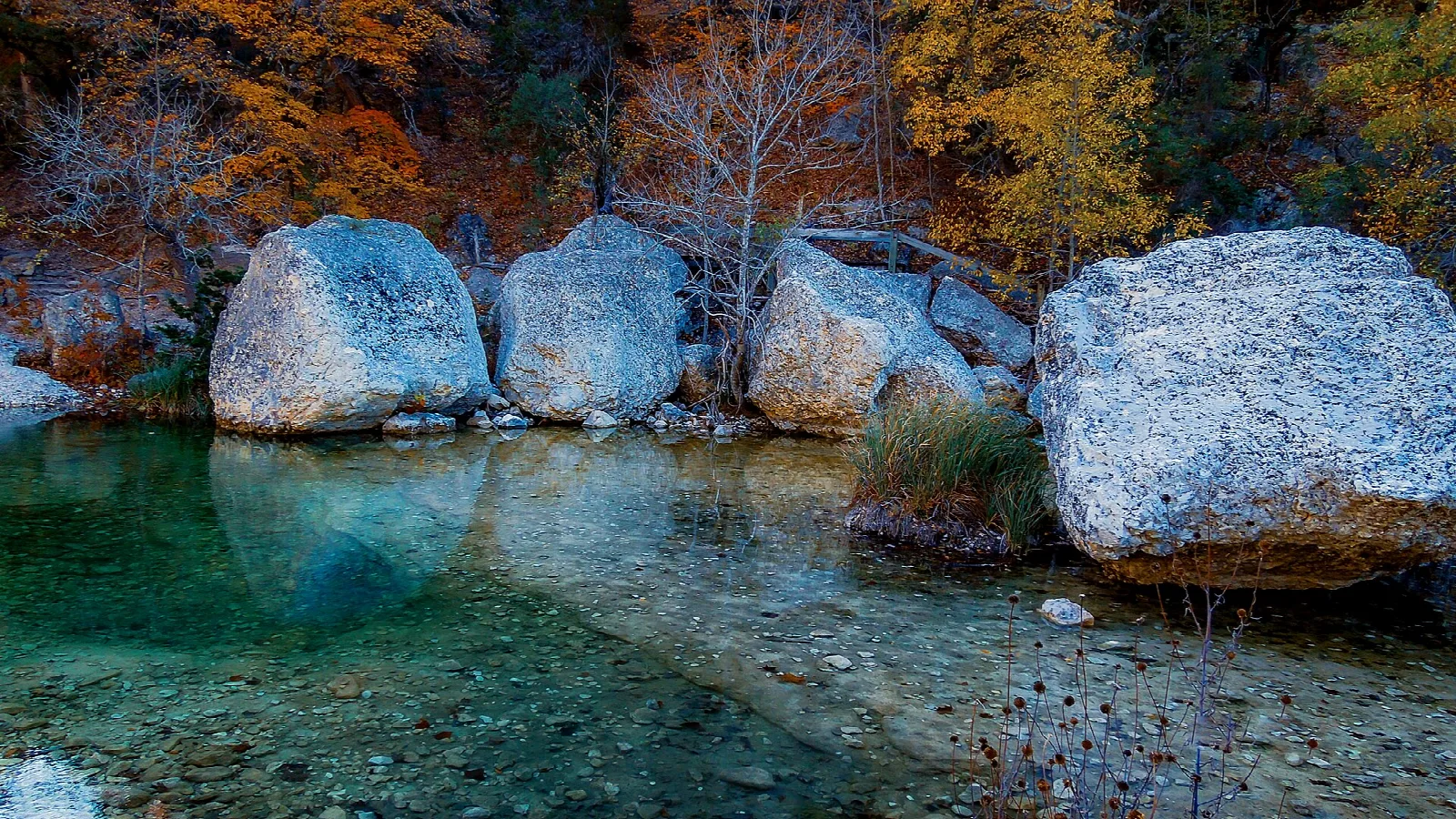 Clear green pool lined with large pale boulders and fall trees