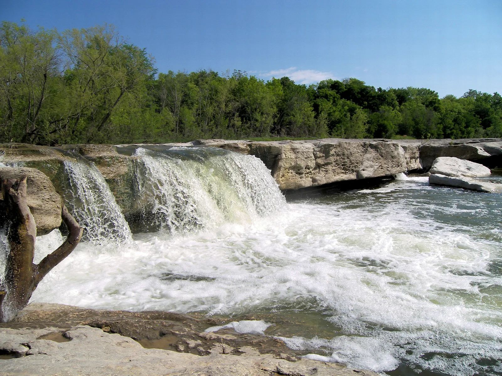 Water cascading over a wide limestone ledge into a rushing creek
