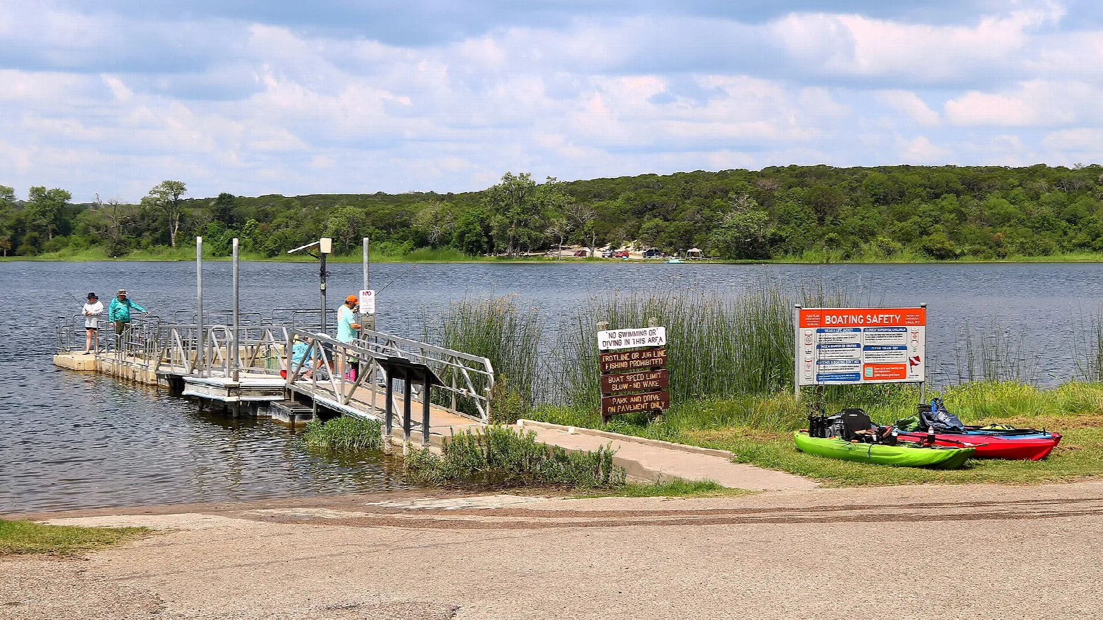 People on a boat dock with kayaks beside a lake