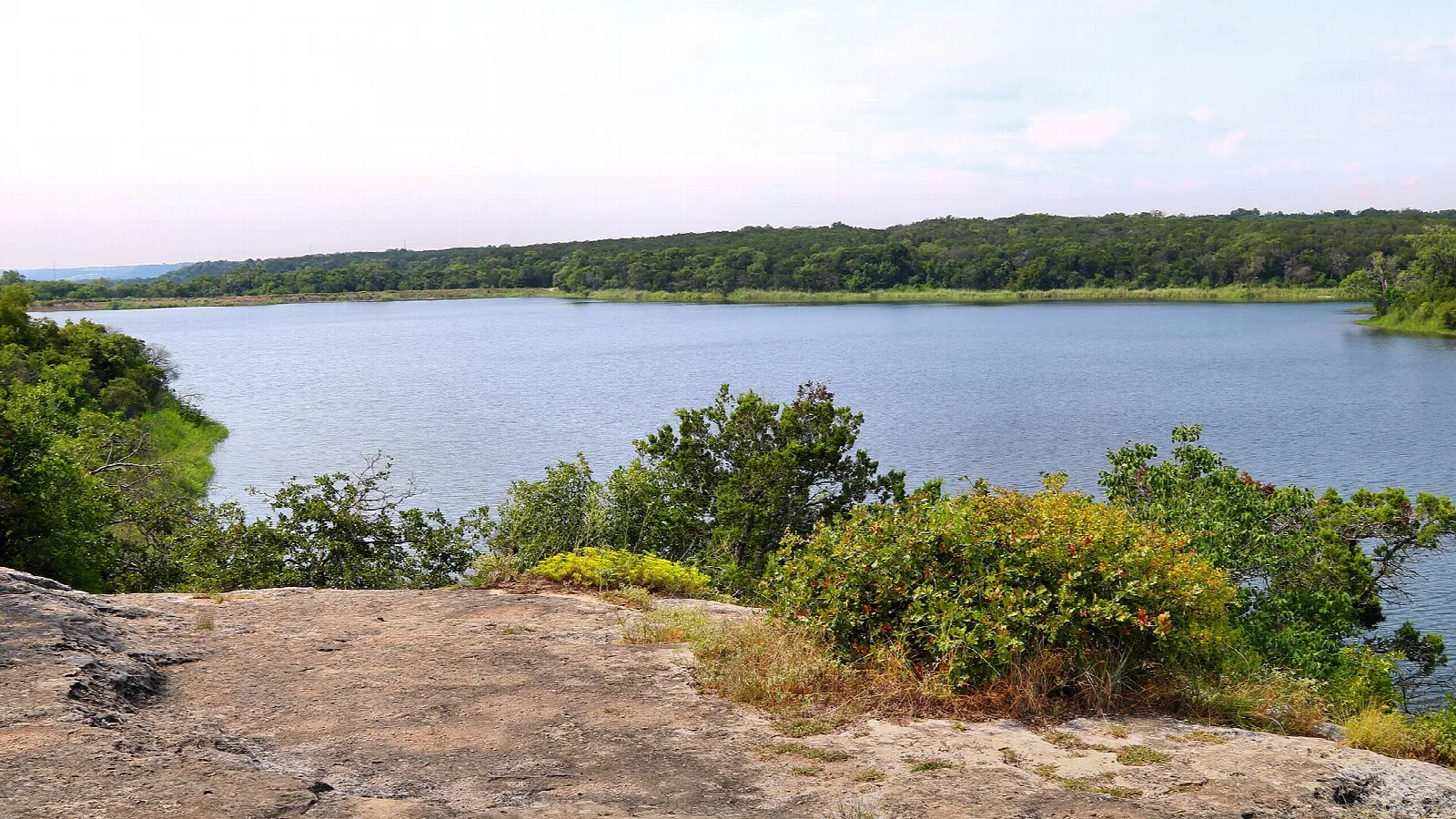 Calm lake seen from a rocky overlook ringed with green shrubs