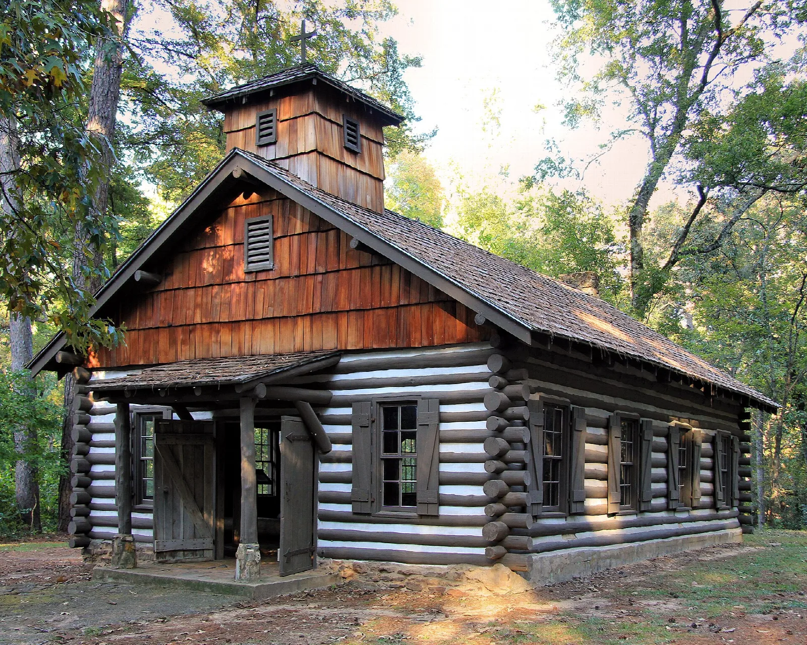 Log chapel with a cupola and shingled roof among pine trees