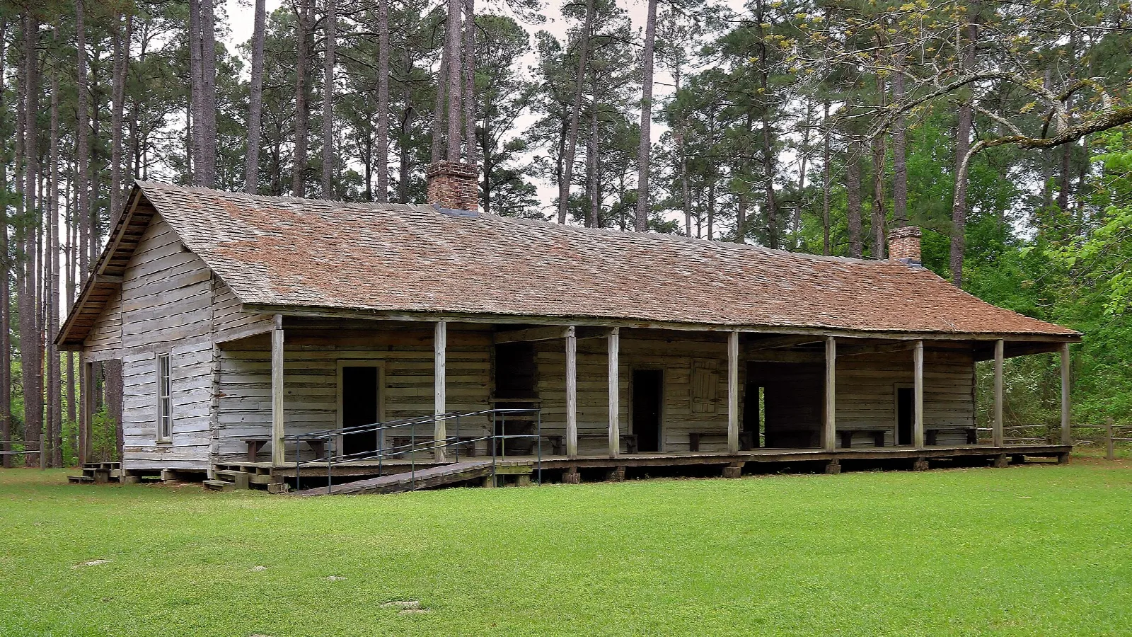 Long wooden cabin with a porch in a pine forest clearing