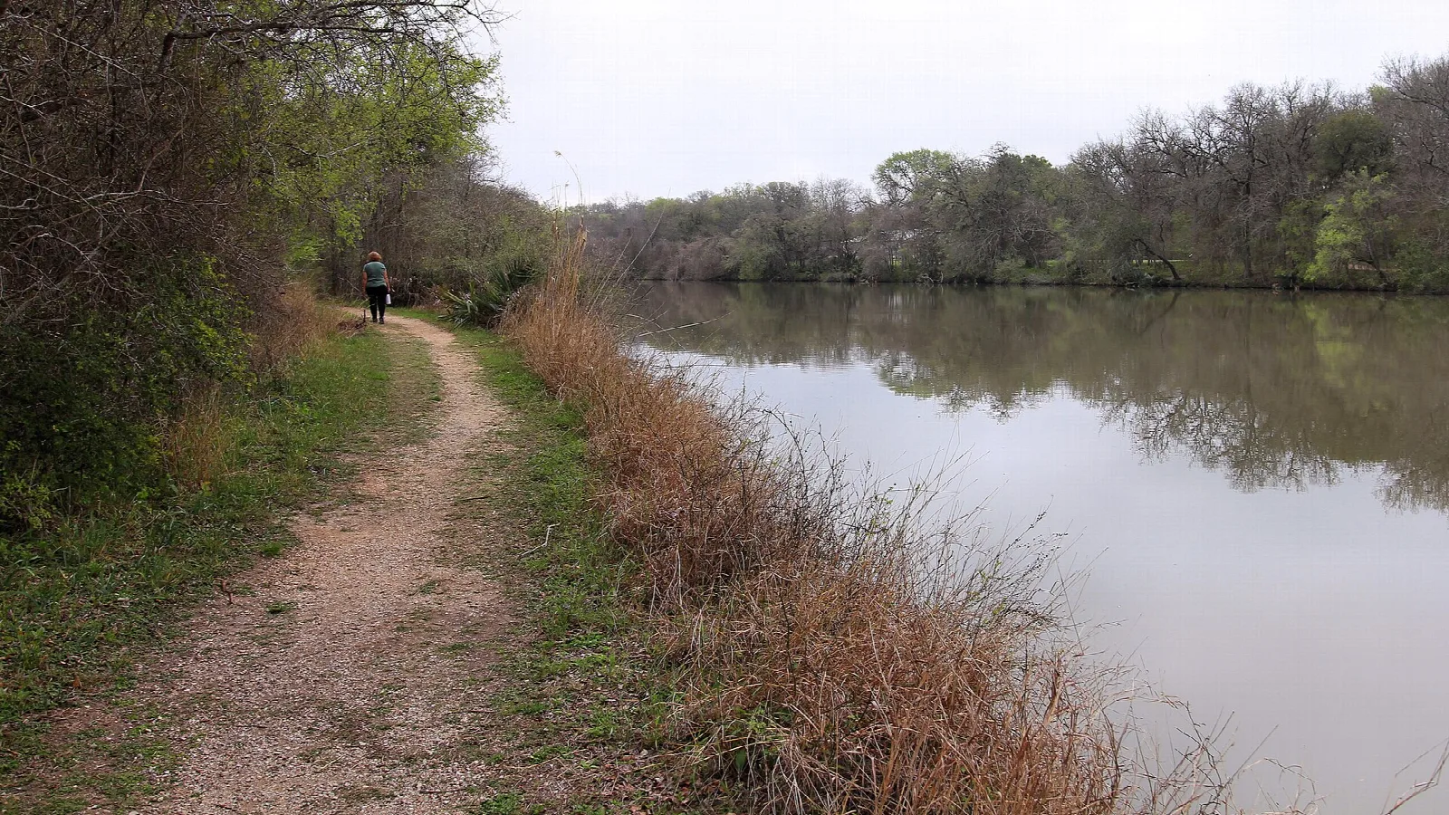 Dirt trail with a hiker beside a lake