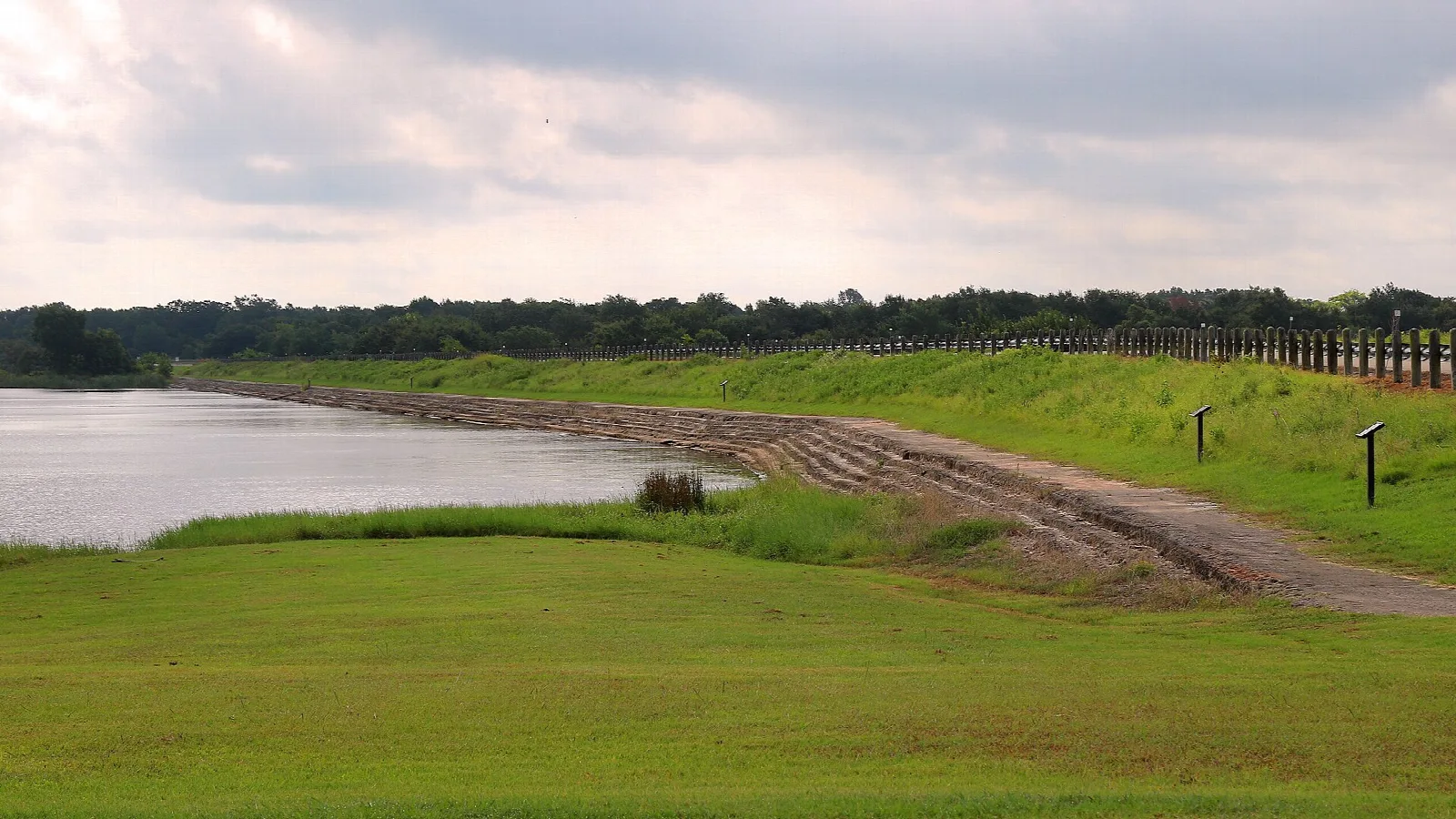 Grassy earthen dam beside a lake under clouds