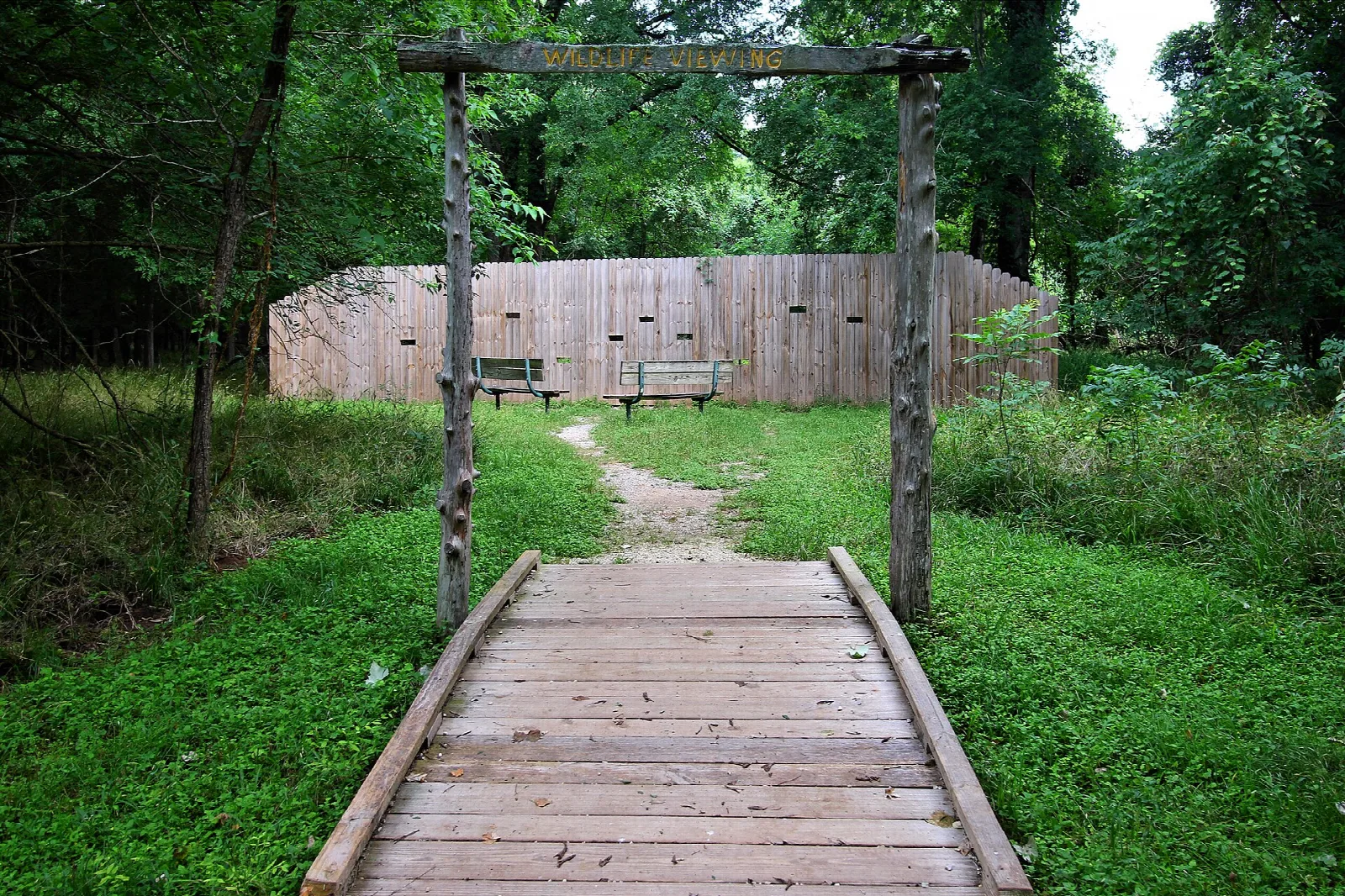 Plank path through a log gate toward a tall wooden wall