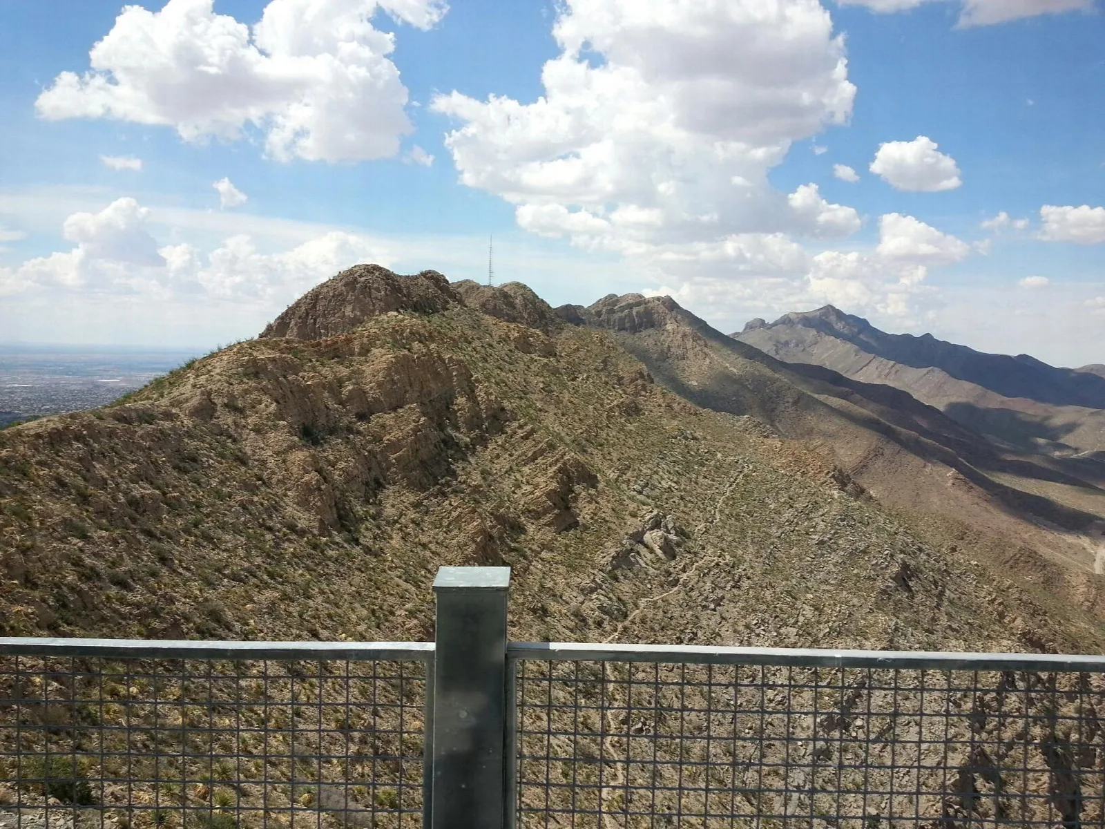 Rugged mountain ridge seen from a railed overlook under puffy clouds